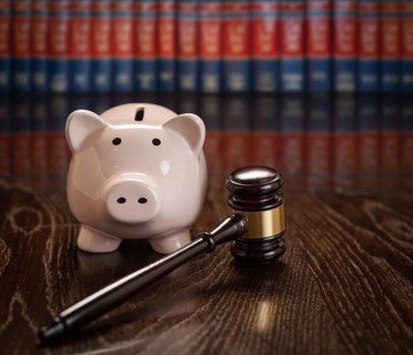 Gavel and piggy bank on wooden table with law books in background