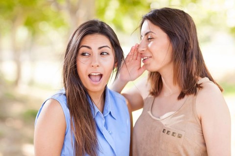 Two beautiful ethnic twin sisters whispering secrets outdoors
