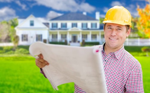 Smiling contractor holding blueprints in front of beautiful custom home