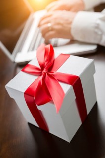 White gift box with red ribbon and bow near man typing on laptop computer