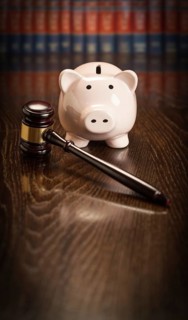 Gavel and piggy bank on wooden table with law books in background