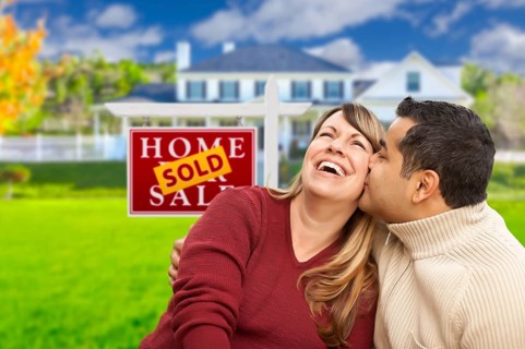 Happy mixed-race couple in front of sold real estate sign