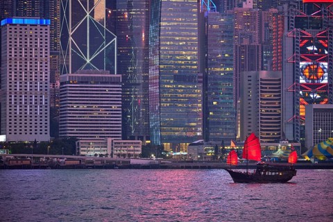 Tourist junk boat ferry with red sails and Hong Kong skyline cityscape downtown skyscrapers over Victoria Harbour in the evening. Hong Kong