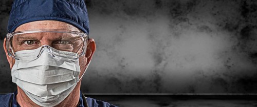 Male doctor or nurse wearing goggles and face mask against grungy dark background banner
