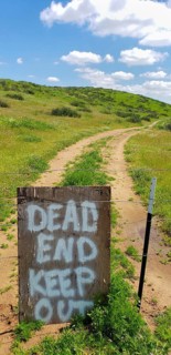 Dead end keep out sign on wire fence at dirt road