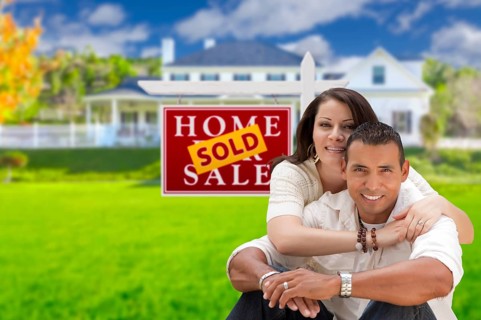 Young happy hispanic young couple in front of their new home and sold for sale real estate sign