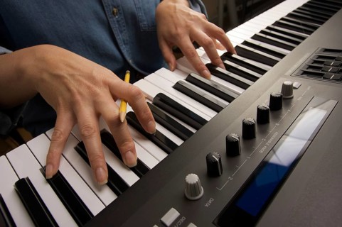Woman's fingers with pencil on digital piano keys