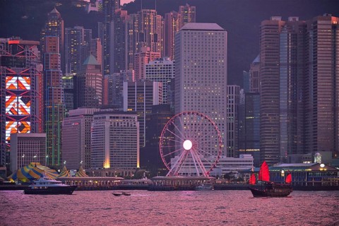 Tourist junk boat ferry with red sails and Hong Kong skyline cityscape downtown skyscrapers over Victoria Harbour in the evening. Hong Kong