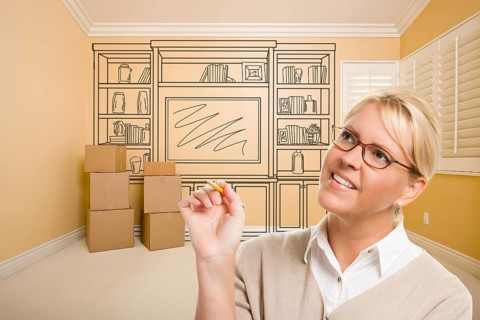 Female holding pencil in room with moving boxes and drawing of entertainment unit on wall