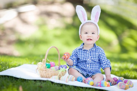 mixed-race chinese and caucasian baby boy outside wearing rabbit ears playing with easter eggs