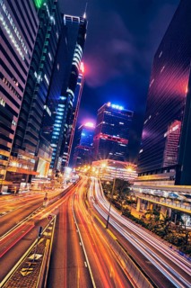 Street traffic in Hong Kong at night. Office skyscraper buildings and busy traffic on highway road with blurred cars light trails. Hong Kong