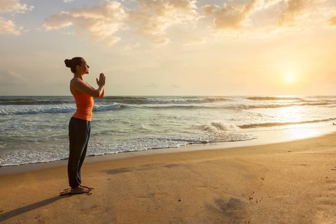 Woman doing Ashtanga Vinyasa Yoga asana Tadasana Samasthiti yoga posture on beach on sunset
