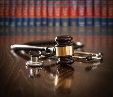 Gavel and stethoscope on wooden table with law books in background