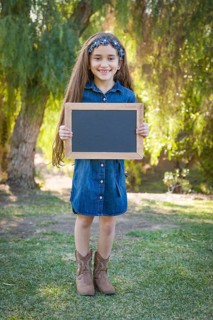 Cute young mixed-race girl holding blank blackboard outdoors