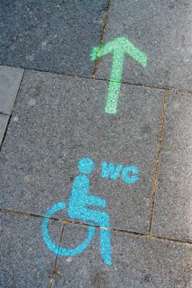 A green arrow with a blue pictogram for a wheelchair-accessible toilet points the way to a disabled toilet on the floor of the pedestrian zone