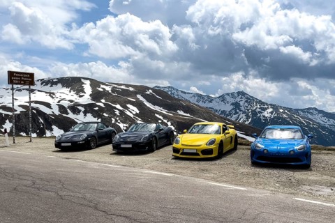 Porsche sports car and Renault Alpine standing at the top of mountain pass in Alps