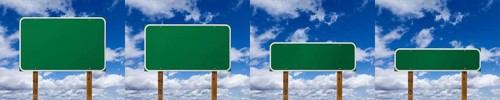 Set of different sized blank green road signs over clouds and blue sky