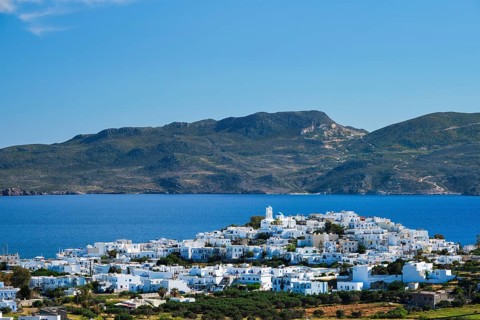 View of Plaka village with traditional Greek orthodox church and white painted houses and ocean coast. Milos island