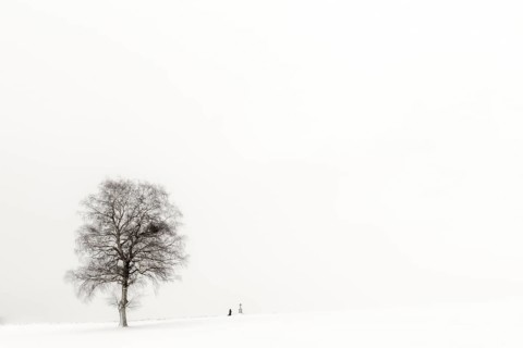 Einsame Frau knieend an Marterl mit Baum in Winterlandschaft