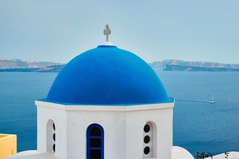 Famous view from viewpoint of Santorini Oia village with blue dome of whitewashed greek orthodox Christian church of traditional greek architecture