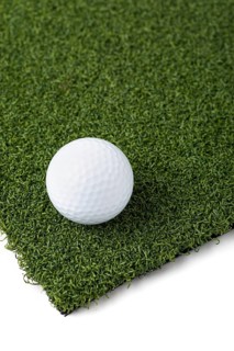 Golf ball resting on section of artificial turf grass on white background