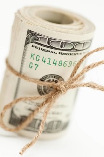 Roll of one hundred dollar bills tied in burlap string on white