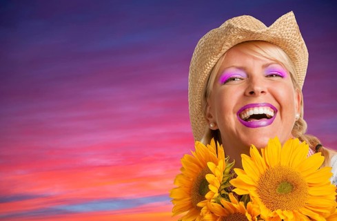 Beautiful laughing girl wearing cowboy hat holding yellow sunflowers against purple and pink sunset