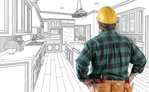 Male contractor with hard hat and tool belt looking at custom kitchen drawing on white