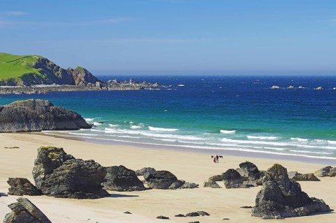 Langer Sandstrand mit einzelnen Felsen und Klippen