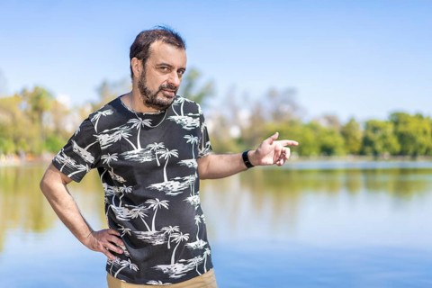 Bearded mature man in a lake looking at the camera with one arm akimbo and the other pointing to the side. Copy space