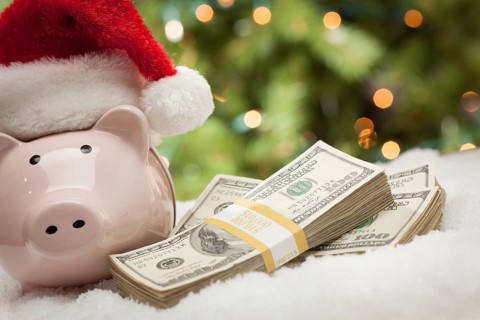 Piggy bank wearing santa hat near stacks of hundred dollar bills on snowflakes