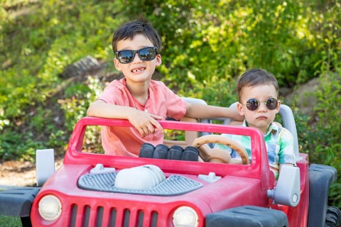 Young mixed-race chinese and caucasian brothers wearing sunglasses playing in toy car