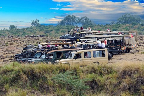 Safari cars on the Mara River with tourists waiting for gnu migration