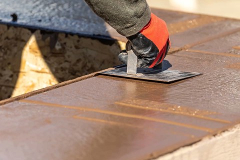 Construction worker using hand groover on wet cement forming coping around new pool
