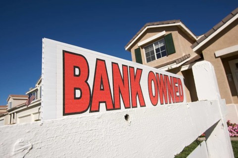 Bank owned real estate sign and house with american flag in the background