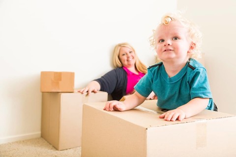Playful happy mother and son in empty room with moving boxes