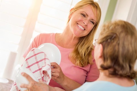 Senior adult woman and young daughter talking at sink in kitchen