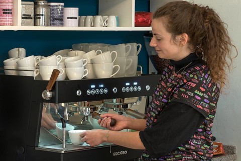 Junge Frau bereitet Kaffee an einer Espressomaschine in einem Cafe