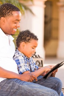 African american father and mixed-race son using computer tablet on bench in park