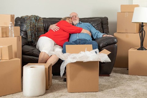 Affectionate tired senior adult couple resting on couch surrounded by moving boxes
