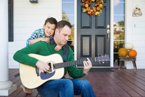Young mixed-race chinese and caucasian son singing songs and playing guitar with father