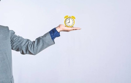 A hand holding a table clock on isolated background