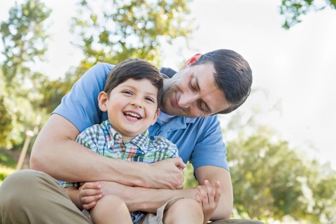 Loving young father tickling son in the park