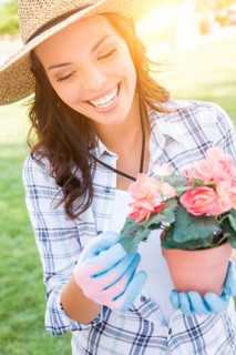 Happy young adult woman wearing hat and gloves gardening outdoors