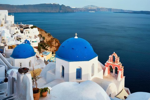 Famous view from viewpoint of Santorini Oia village with blue dome of whitewashed greek orthodox Christian church of traditional greek architecture