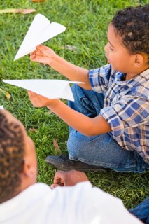 Happy african american father and mixed-race son playing with paper airplanes in the park
