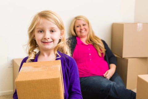 Happy young mother and daughter in empty room with moving boxes