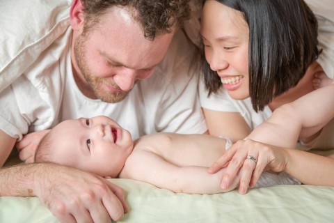 mixed-race chinese and caucasian baby boy laying in bed with his father and mother