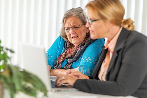 Woman helping senior adult lady on laptop computer