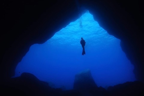Diver floating in open water in front of large cave entrance of underwater cave